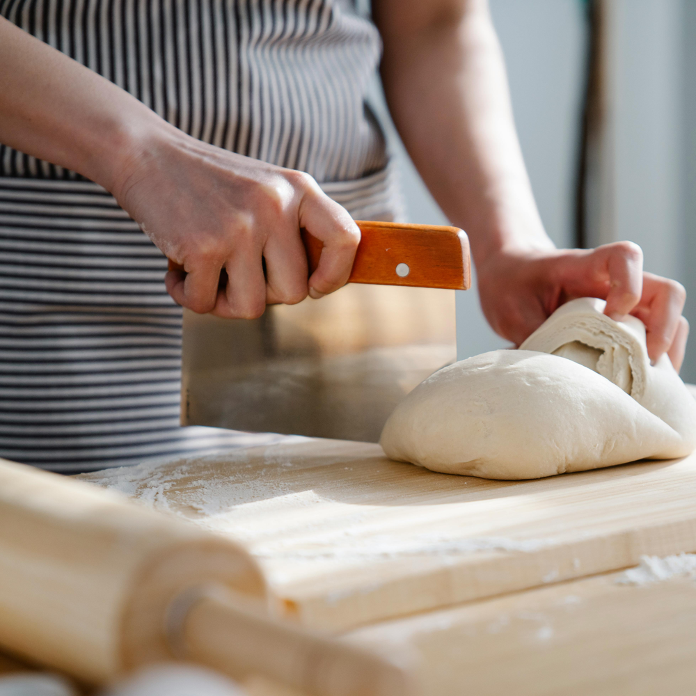 A person slicing pasta dough using a dough scraper