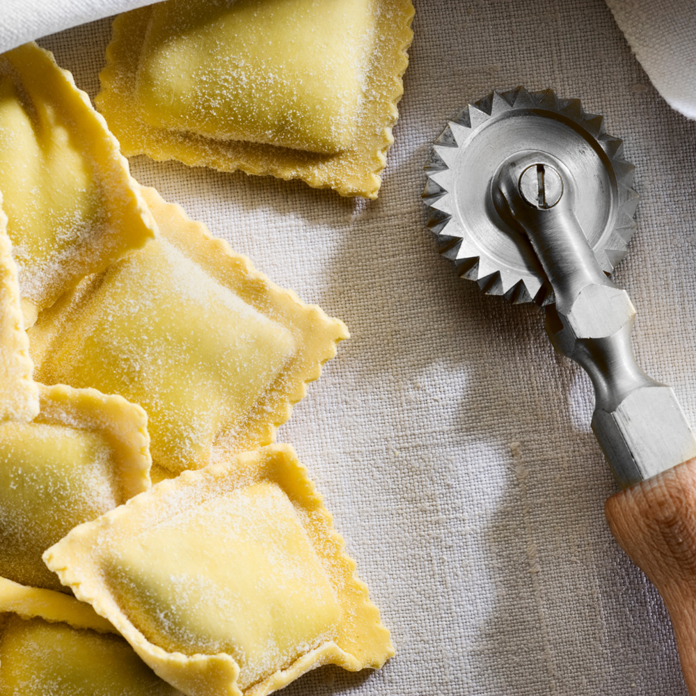 A pasta wheel cutter next to fresh cut ravioli