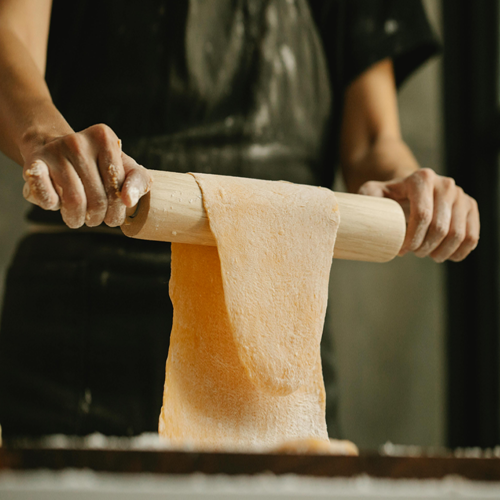 A man holding a rolling pin with pasta dough gently laid over it.